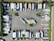 An aerial view of a parking lot filled with trucks and trailers arranged in rows. The vehicles are organized in a systematic manner, with some smaller cars and trailers mixed in. Trees and small green spaces are distributed throughout the area, providing some greenery amid the concrete.