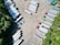 Aerial view of a parking area filled with several semi-trailers, arranged in neat rows. The trailers are primarily white, with a few in different colors such as red, blue, and green. The area is surrounded by greenery, with trees lining the lot on one side.