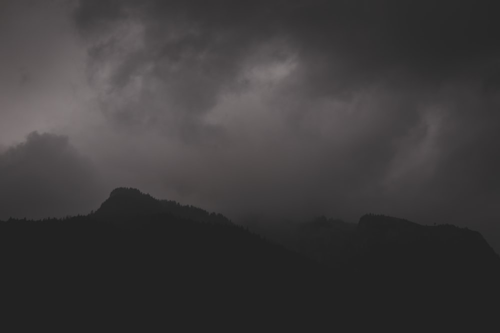 a black and white photo of a mountain under a cloudy sky