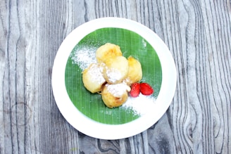 A colorful plate featuring a coconut tart, pineapple cake, and banana fritters arranged on a tropical leaf.