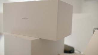 Stacked white boxes with minimalistic design featuring a label 'COLLECTION 1'. The setting appears to be clean and well-organized, possibly in a storage or retail environment.