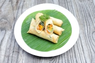 Freshly made spring rolls arranged neatly on a rustic wooden plate.