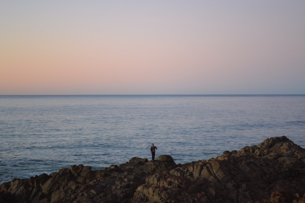 a person standing on a rocky shore next to the ocean