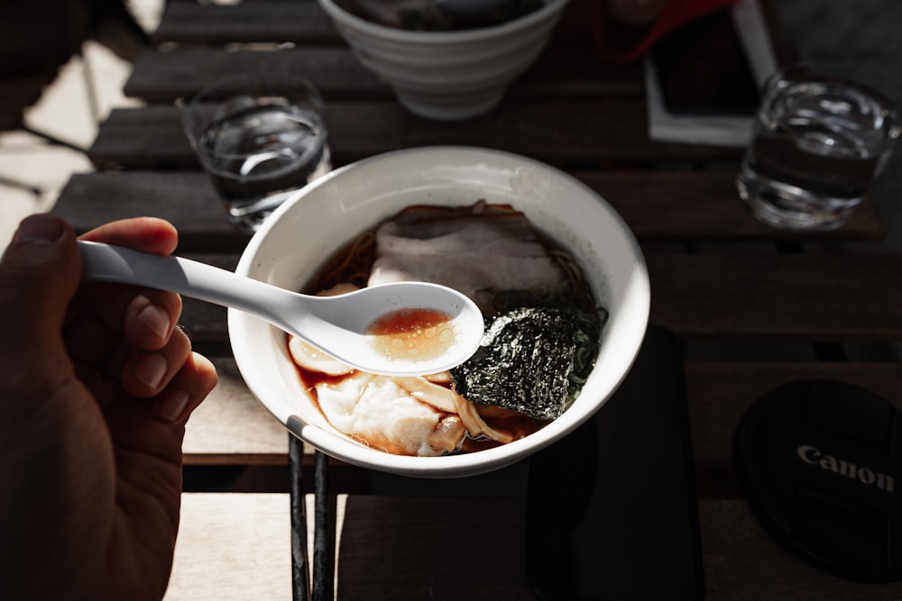 a person holding a spoon over a bowl of food