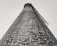 A tall brick chimney stretches skyward, captured from a low angle. The brickwork is detailed, with metal rungs attached along the side for climbing. The perspective creates a sense of height and scale.