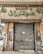 A closed storefront with metal shutters, surrounded by stone-patterned walls. The sign above the entrance features Arabic script in large green letters. The shop appears to be located on a narrow street with a parked car partially visible on the left. The exterior shows signs of wear and age, with peeled paint and weathered surfaces.