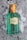 A green glass bottle of Gucci Mémoire d'une Odeur perfume is resting on the snow. The bottle has a textured design with a golden cap, and a label in the center featuring the brand and product name.