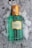 A green glass bottle of Gucci Mémoire d'une Odeur perfume is resting on the snow. The bottle has a textured design with a golden cap, and a label in the center featuring the brand and product name.