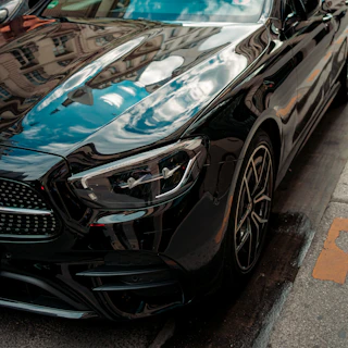 Close-up of a sleek black luxury car with a glossy, freshly detailed exterior reflecting the Oakland skyline.