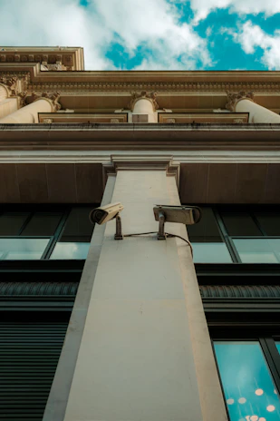 An architectural shot of a fortified building entrance with advanced surveillance cameras discreetly positioned.