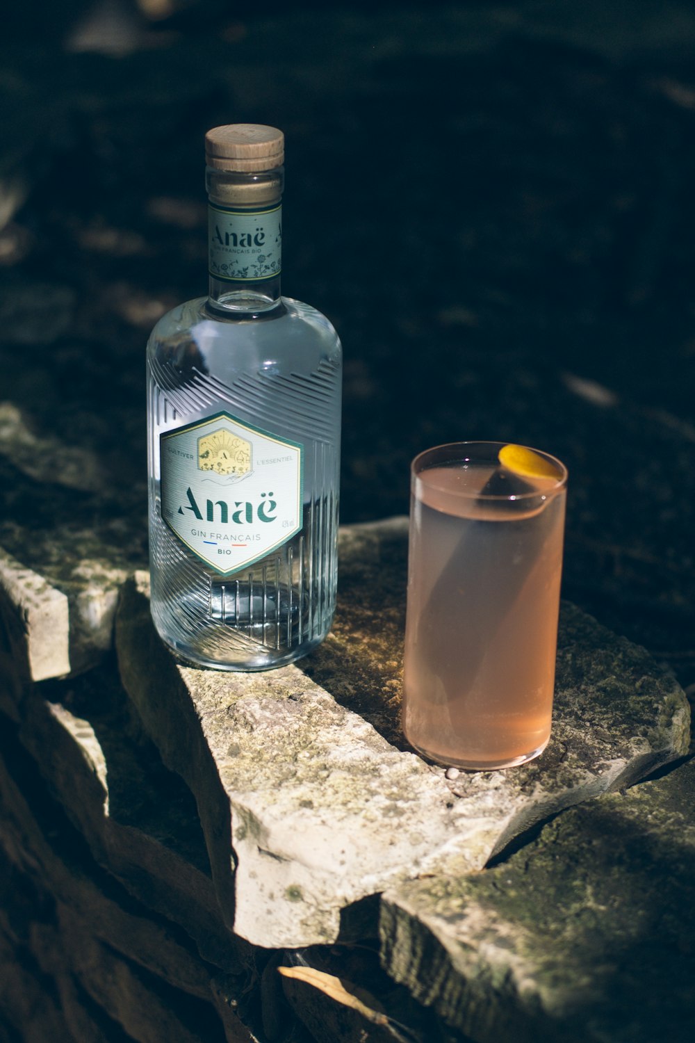 a bottle of alcohol next to a glass on a rock