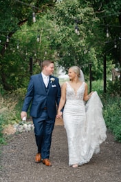 a bride and groom walking through the woods
