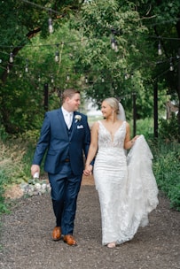 a bride and groom walking through the woods