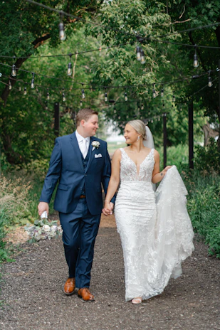 Softly lit photo of Adrianna and Lucas walking hand in hand along a garden path lined with powder blue blooms.