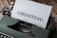 A vintage typewriter with a sheet of paper inserted showing the word 'GHOSTING' in bold letters. The typewriter is placed on a wooden surface, and the image has a retro aesthetic.