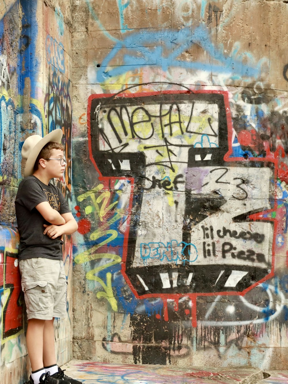 a young boy standing in front of a wall covered in graffiti