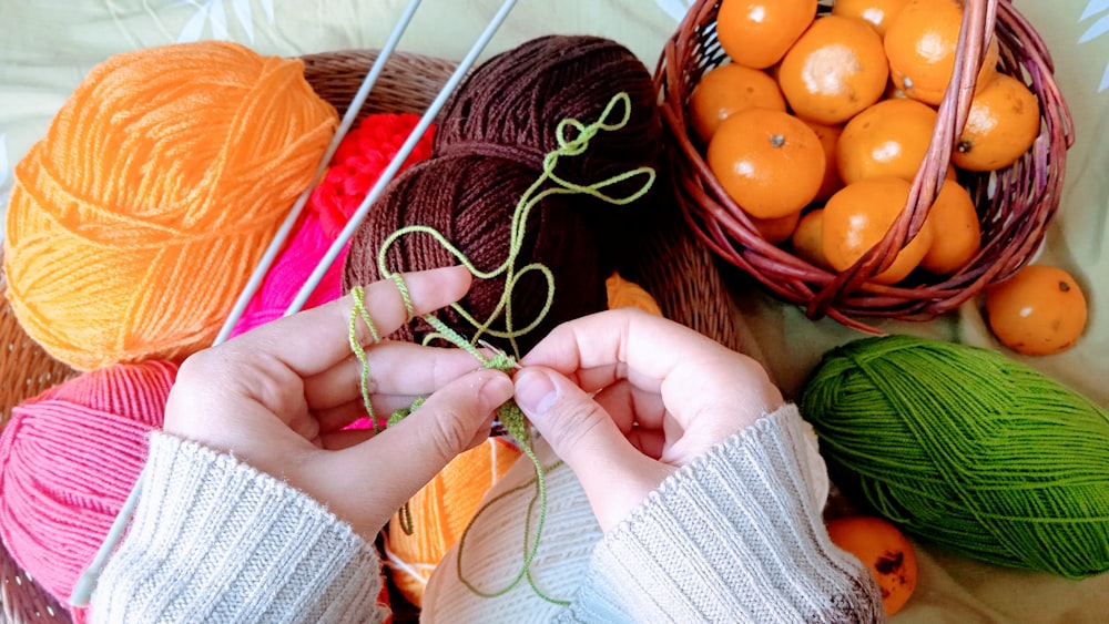 a person knitting yarn with oranges in the background