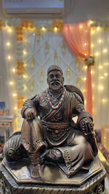 A bronze statue of King Kosoko, illuminated by deep royal blue and antique gold lighting, symbolizing enduring legacy.