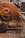 A close-up view of an industrial circular saw in motion, cutting through metal or a similar material, producing sparks that fly in various directions. The saw is predominantly orange and appears to be weathered. The surrounding area has a gritty, construction-like environment with scattered debris.