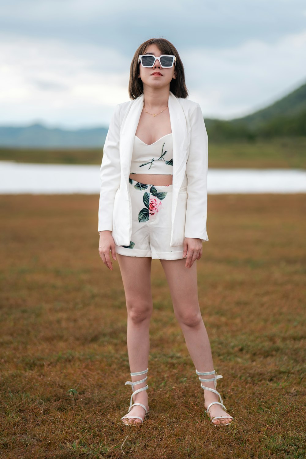 a woman standing in a field wearing a white suit and sunglasses