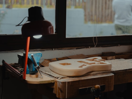 A worn acoustic guitar undergoing neck realignment on a sturdy workbench.