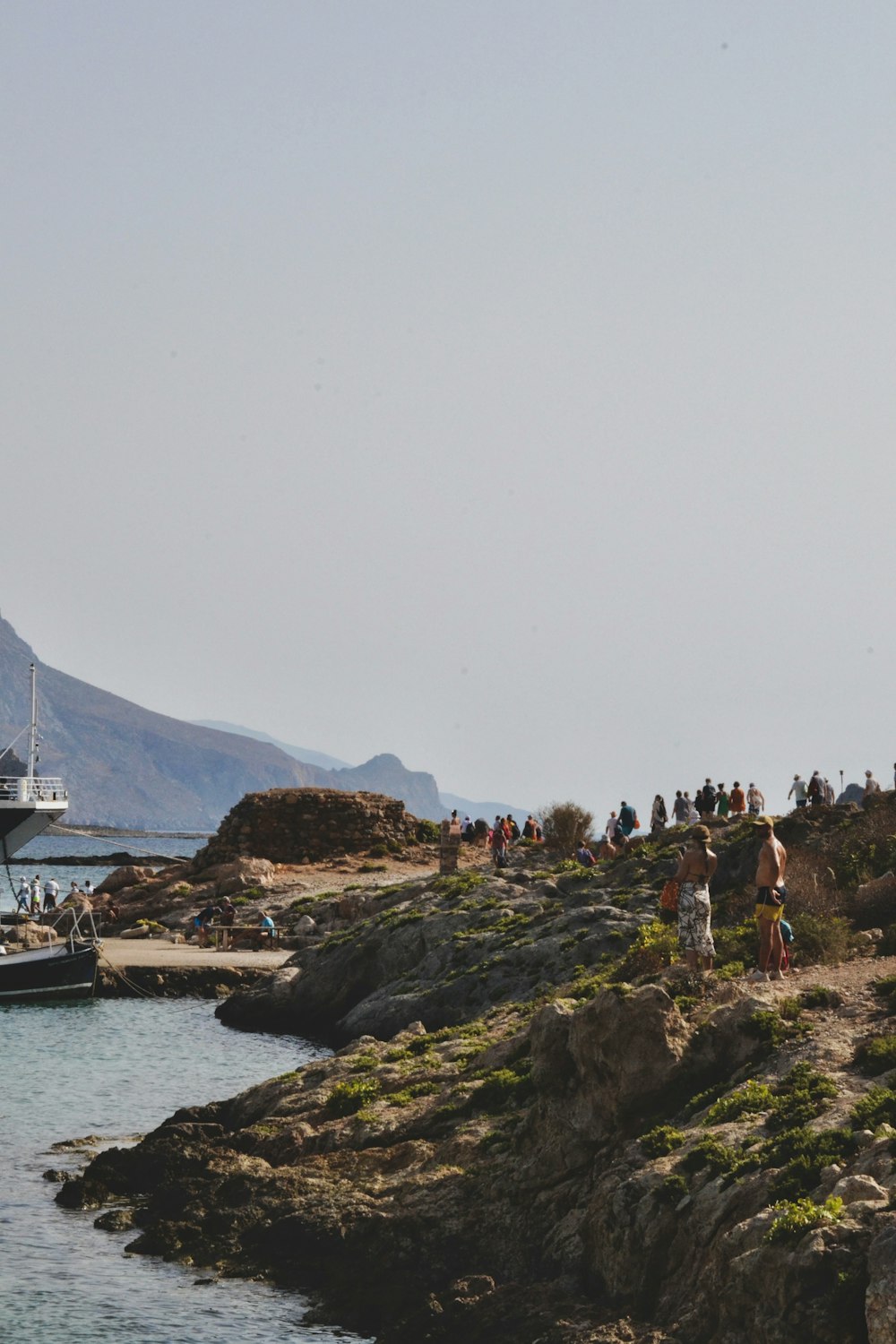 a group of people standing on top of a cliff next to a body of water