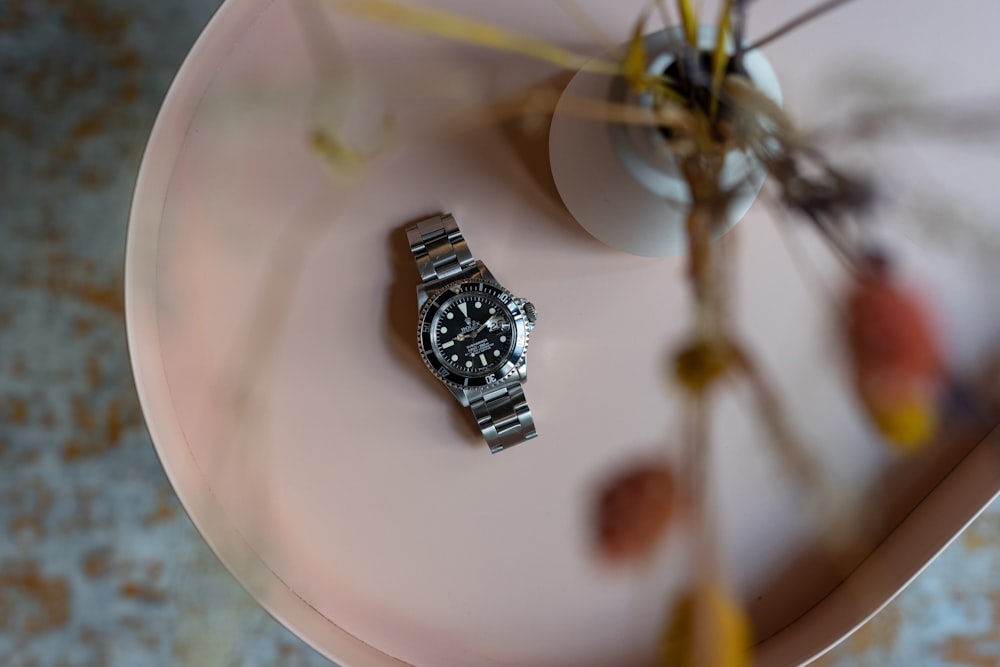 a watch sitting on a plate next to a flower