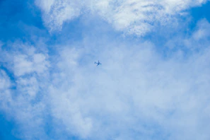 A small plane soaring high above patchwork fields under a vast blue sky
