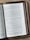 A close-up of an open book placed on a wooden surface. The book appears to be a Bible, featuring text primarily in black font on white pages with a reference to 'LUKE 10-11'. The edges of the book have a red tint, and the book has a brown leather cover.