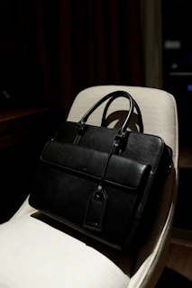 A sleek black travel bag resting on a sunlit airport bench with a boarding pass peeking out