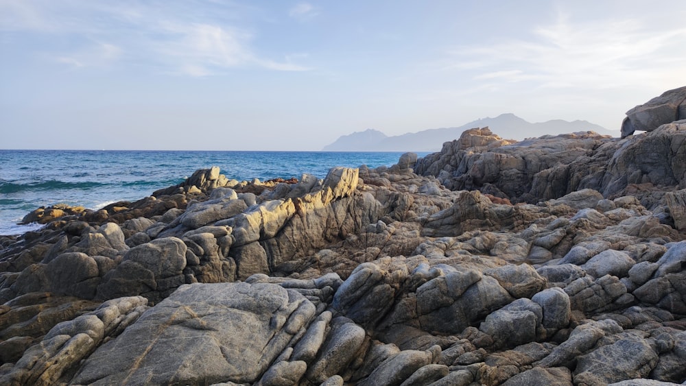 a rocky shore line with water and mountains in the background