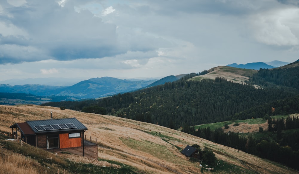 une petite cabane sur une colline herbeuse avec des montagnes en arrière-plan