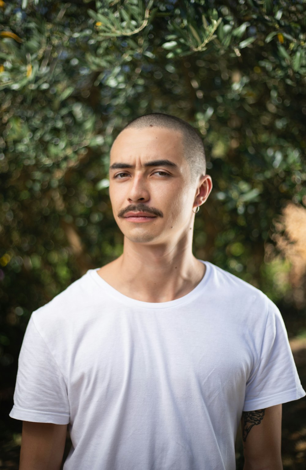 a man with a mustache standing in front of a tree