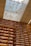 A library with towering wooden bookshelves filled with books and illuminated by warm lights. Above, a glass ceiling lets in natural light and features artistic paper-like sculptures suspended in motion, creating a sense of whimsical movement.