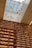A library with towering wooden bookshelves filled with books and illuminated by warm lights. Above, a glass ceiling lets in natural light and features artistic paper-like sculptures suspended in motion, creating a sense of whimsical movement.
