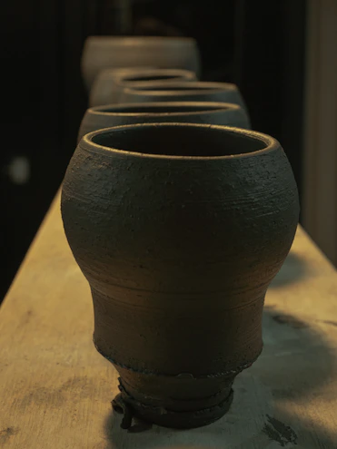 Handcrafted ceramic pots arranged on a rustic wooden shelf with natural light highlighting their textures