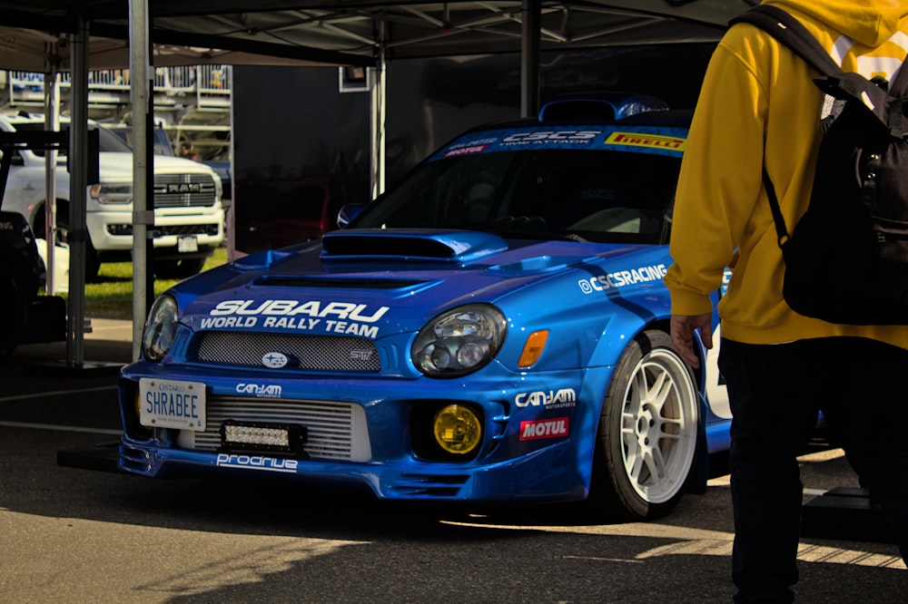 a man in a yellow hoodie standing next to a blue car