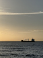 A large cargo ship cutting through calm ocean waves at sunrise.