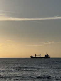 A sleek cargo ship cutting through calm ocean waters under a clear sky at sunrise.