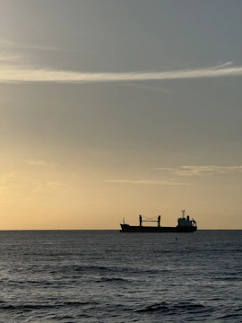 Close-up of a cargo ship navigating through calm ocean waters at sunrise.