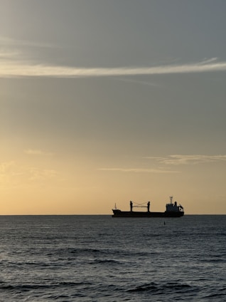 A calm ocean horizon with a cargo ship silhouette at sunset.