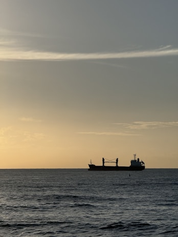 A large oil tanker ship navigating through calm ocean waters at sunset