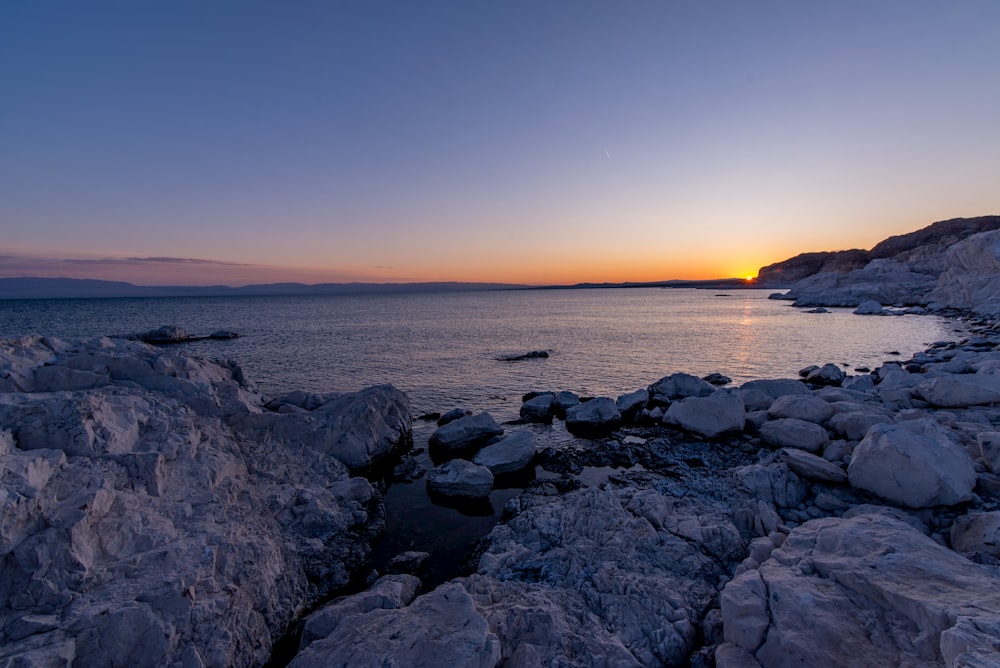 the sun is setting over a rocky beach