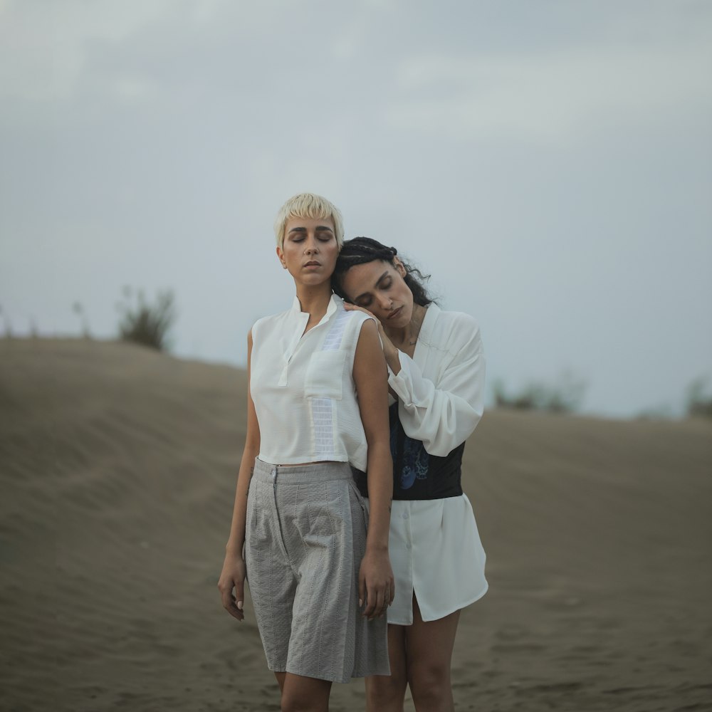 two women standing in the sand with their arms around each other