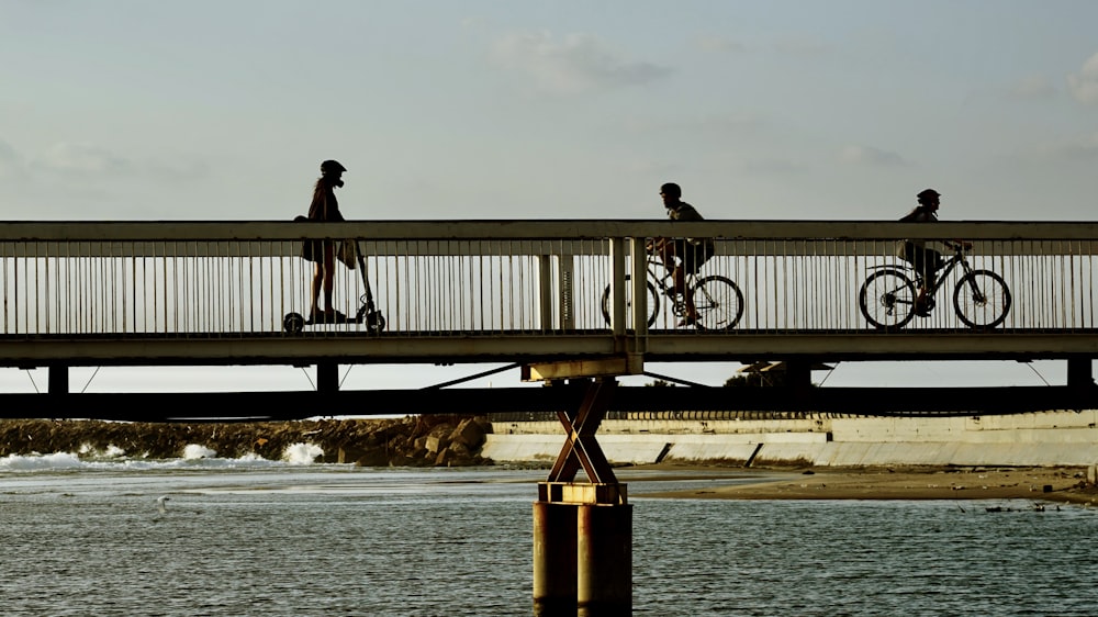 a group of people riding bikes across a bridge over a body of water