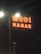 The image features a large, illuminated sign with the words 'MODI NAGAR' displayed in bright red neon lights against a dark background. The sign is positioned on a tall pole with additional light sources visible behind it, casting a glow around the letters.