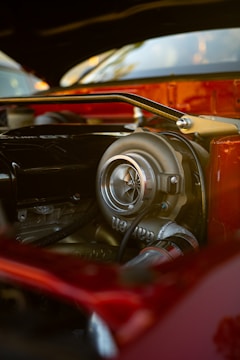 A close-up view of a car engine with prominent focus on a turbocharger. The engine components showcase a mixture of metallic and glossy surfaces, reflecting the surrounding light. The background is slightly blurred, highlighting the details of the engine.