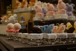 A collection of small, colorful plush animal figurines arranged on rotating display stands. The figures include blue dolphins, brown seals, and other pastel-colored animals like rabbits and birds. They are intricately designed with soft textures, and the display has multiple tiers showcasing the variety.
