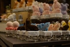 A collection of small, colorful plush animal figurines arranged on rotating display stands. The figures include blue dolphins, brown seals, and other pastel-colored animals like rabbits and birds. They are intricately designed with soft textures, and the display has multiple tiers showcasing the variety.
