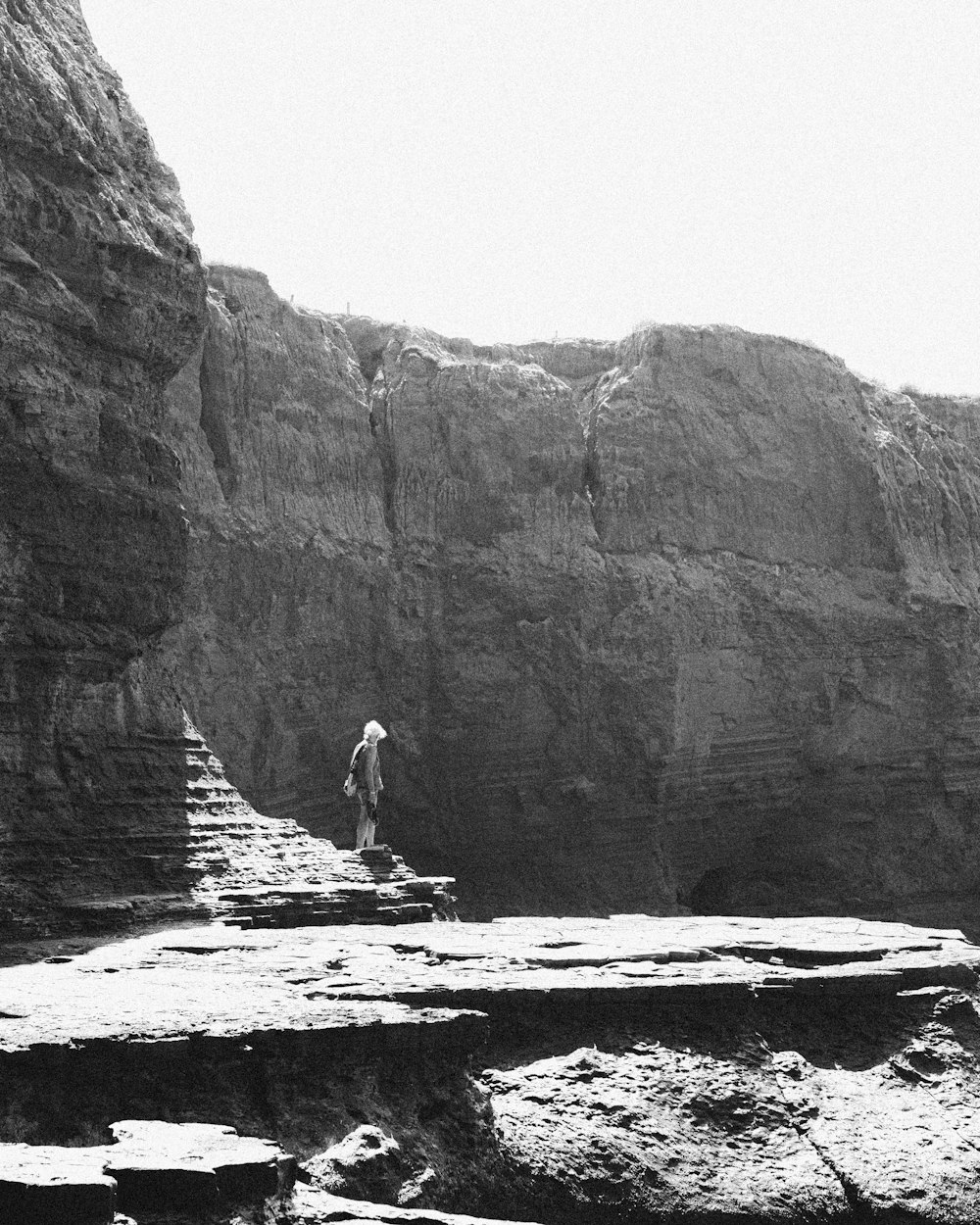 a black and white photo of a man standing on a cliff